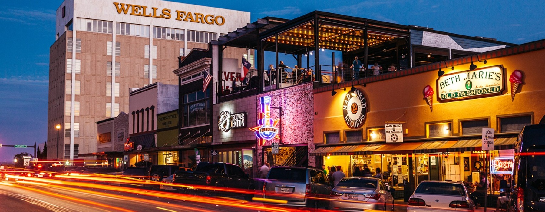 Evening photo of downtown Denton with restaurant signs lit up